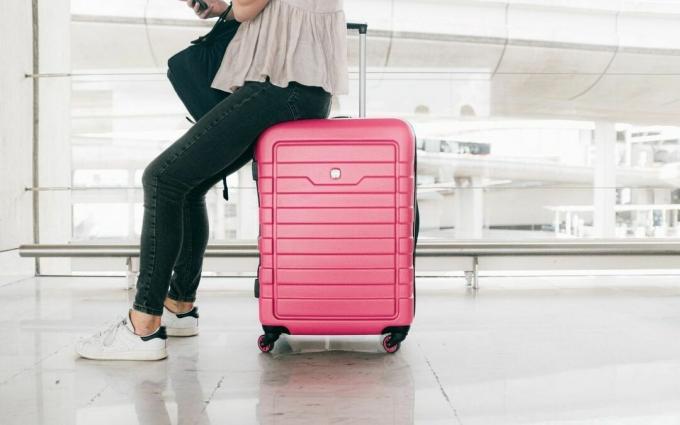 Femme en haut blanc et jeans denim assis sur un sac à bagages rouge