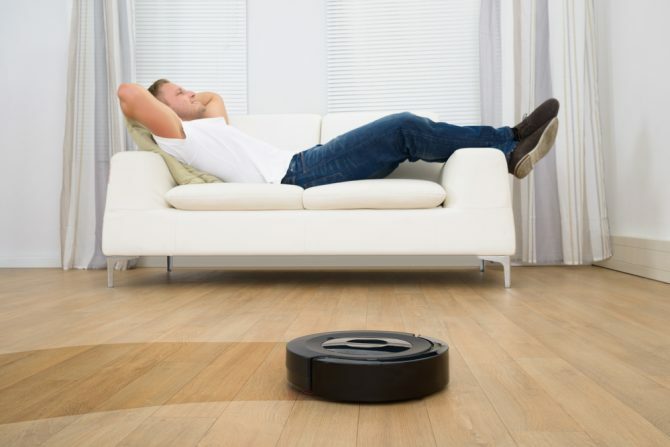 Homme relaxant sur canapé avec aspirateur robotique sur plancher de bois franc